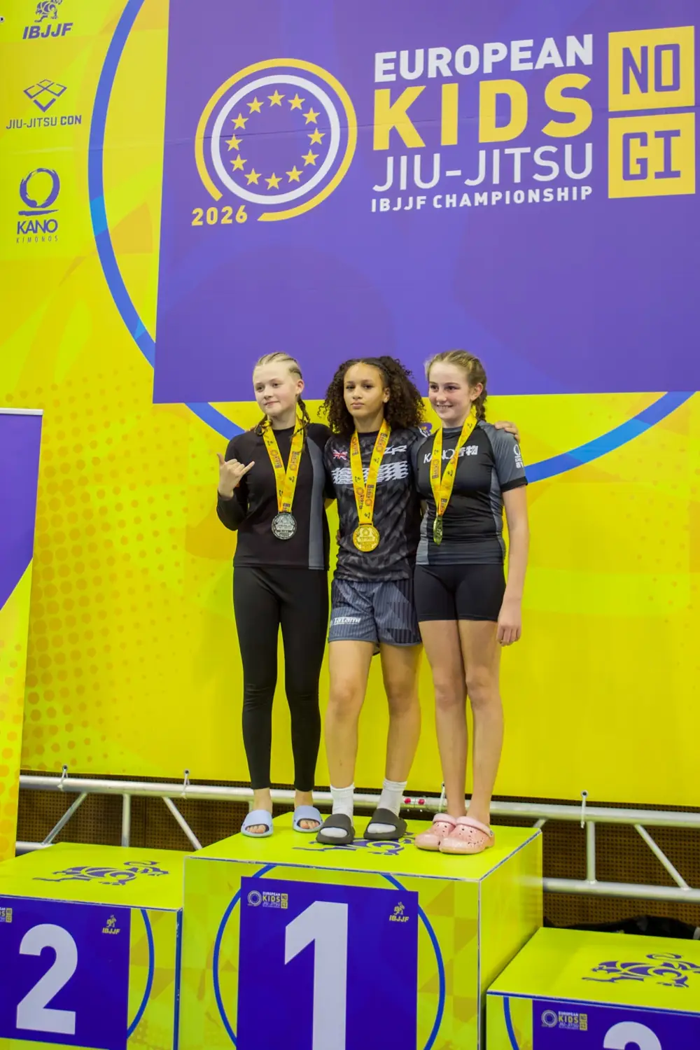 Monét David on the first-place podium alongside the silver and bronze medallists at the 2026 European Kids No-Gi Championships