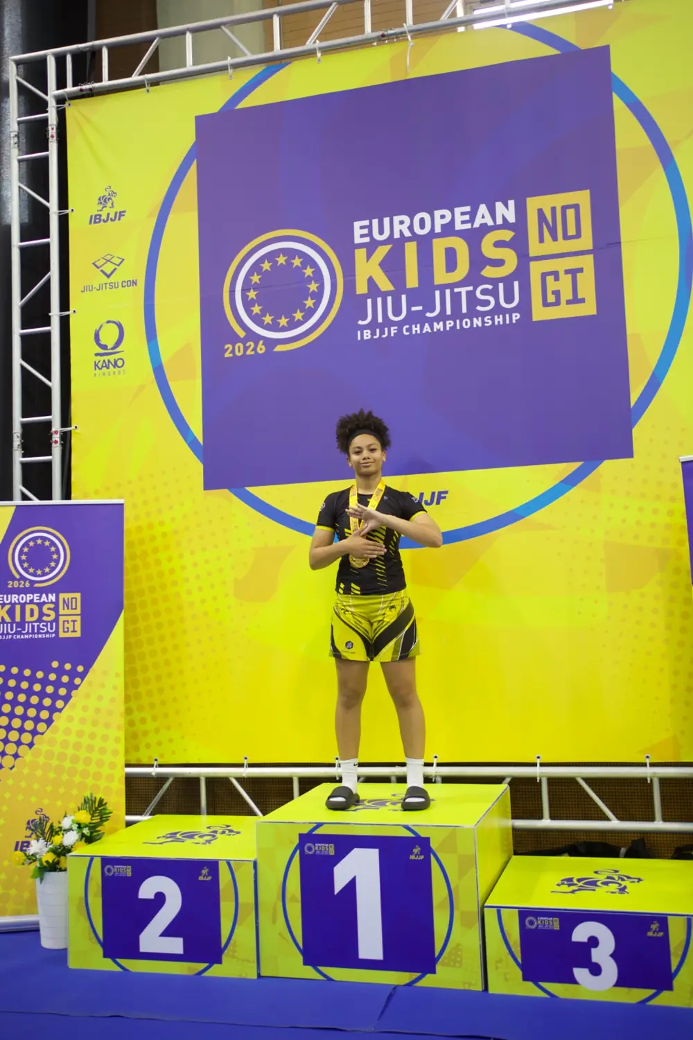Naimah David wearing her gold medal on the first-place podium at the 2026 IBJJF European Kids No-Gi Championships