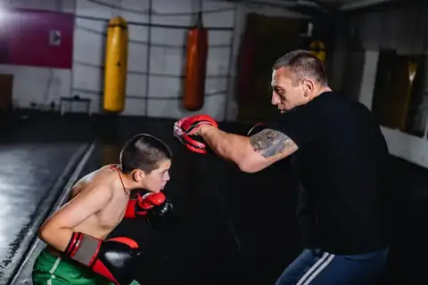 Young kickboxer practising controlled technique with a coach on focus pads